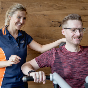 Trainerin unterstützt Mann beim Training an Fitnessgerät im Fitnessstudio für Gesundheit.