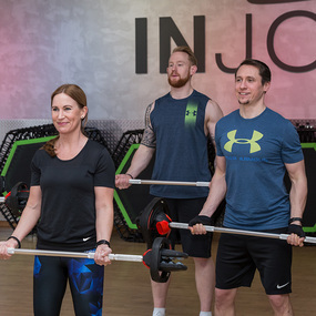 Drei Erwachsene trainieren gemeinsam mit Langhanteln im Fitnessstudio beim Krafttraining.