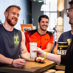 Drei sportliche Männer trinken Proteinshake nach dem Fitnessstudio am Tresen und lachen gemeinsam.