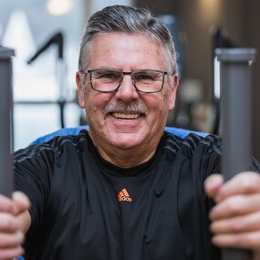 Älterer Mann trainiert lächelnd an einem Fitnessgerät im modernen Fitnessstudio.