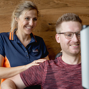 Trainerin unterstützt Mann beim Training an Fitnessgerät im modernen Fitnessstudio.