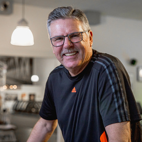 Älterer Mann mit Brille und Sportshirt lächelt in einem modernen Fitnessstudio.