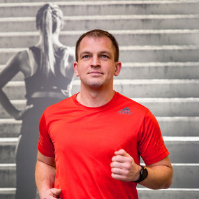 Mann in rotem Sportshirt joggt vor Treppe, Fitness und Ausdauertraining im Fokus.